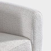 Right facing close up of the inner armrest of a contemporary off-white metallic boucle shelter armchair on a white background
