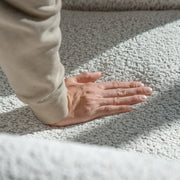 Right facing close up of a person's hand pressing into the seat cushion of a contemporary off-white metallic boucle shelter armchair