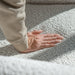 Right facing close up of a person's hand pressing into the seat cushion of a contemporary off-white metallic boucle shelter loveseat