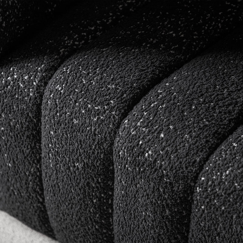 Left facing close up upholstery and tufting of a contemporary black and metallic boucle tufted shelter armchair on a white background