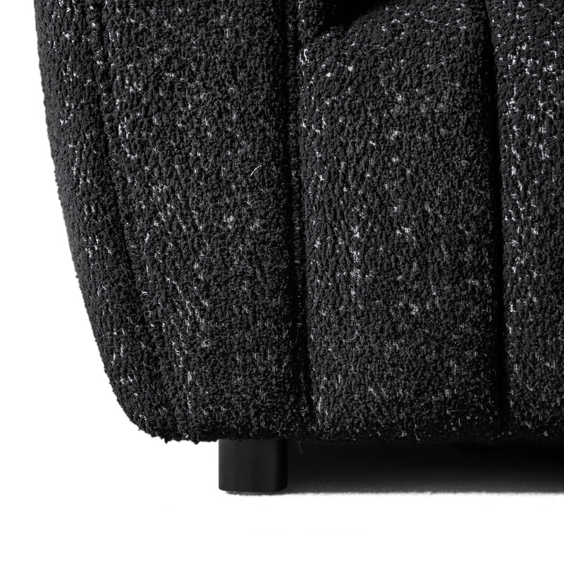 Front facing close up armrest and leg of a contemporary black and metallic boucle tufted shelter sofa on a white background