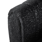 Left facing close up upholstery and rounded armrest of a contemporary black and metallic boucle tufted shelter sofa on a white background
