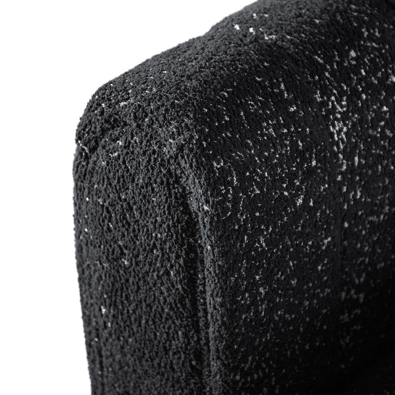 Left facing close up upholstery and rounded armrest of a contemporary black and metallic boucle tufted shelter sofa on a white background