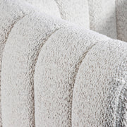 Right facing close up view of the upholstery and tufting on a contemporary off-white metallic boucle tufted shelter armchair on a white background