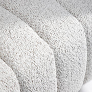 Right facing close up view of the upholstery and tufting on a contemporary off-white metallic boucle tufted shelter armchair on a white background