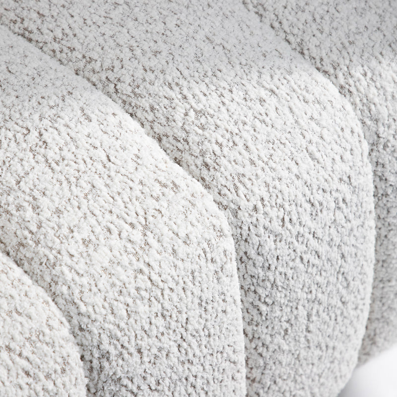Right facing close up view of the upholstery and tufting on a contemporary off-white metallic boucle tufted shelter armchair on a white background