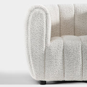 Front facing close up view of the rounded armrest and leg on a contemporary off-white metallic boucle tufted shelter armchair on a white background