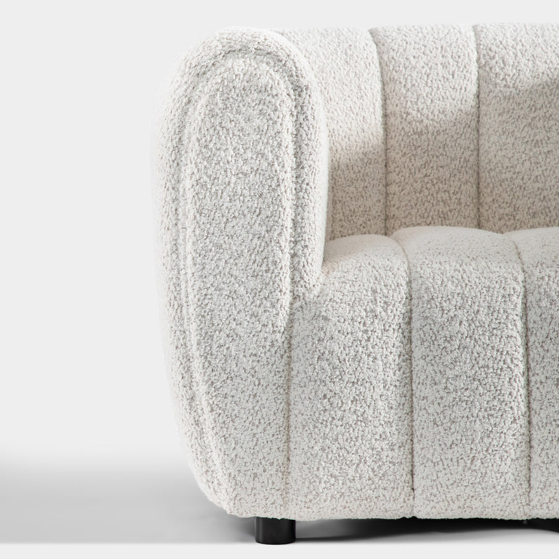 Front facing close up view of the rounded armrest and leg on a contemporary off-white metallic boucle tufted shelter armchair on a white background