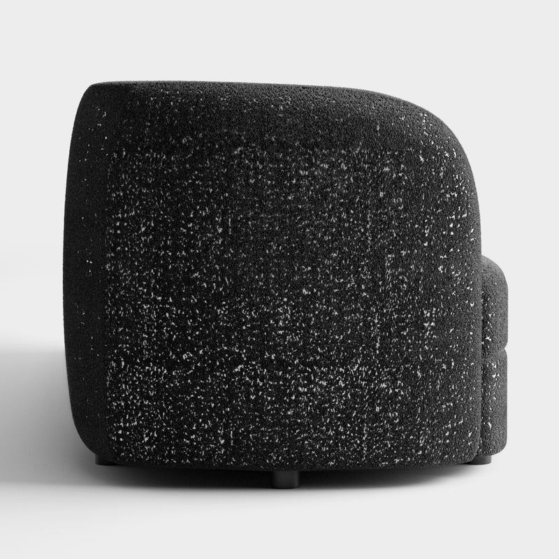 Front facing side view of a contemporary black and metallic boucle curved kidney armchair on a white background