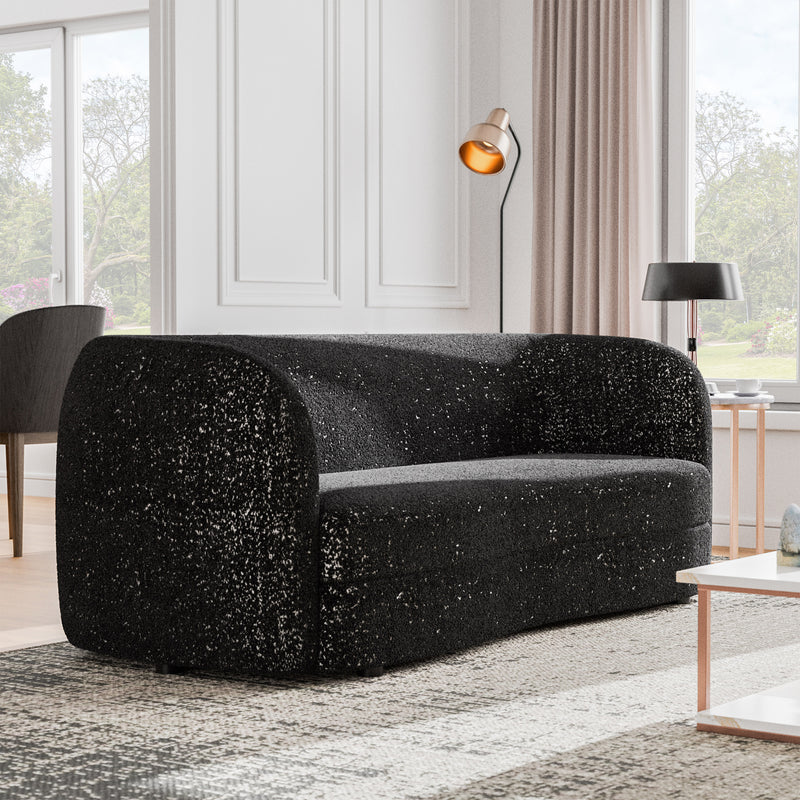 Right facing contemporary black and metallic boucle curved kidney sofa in a living room with accessories