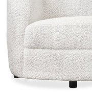 Front facing close up view of the upholstery and leg on a contemporary off-white metallic boucle curved kidney sofa on a white background