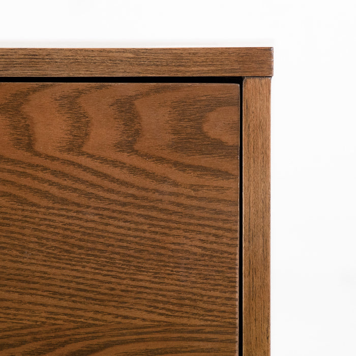 Front facing close up view of the upper corner on a mid-century modern walnut finish five-drawer chest on a white background