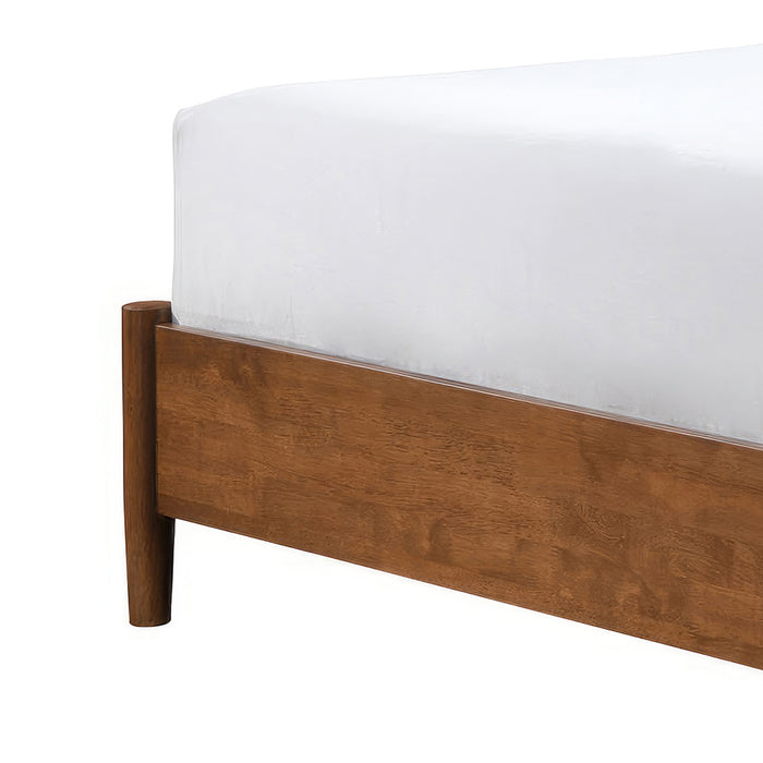 Left facing close up view of the footboard and leg on a mid-century modern walnut finish queen bed on a white background
