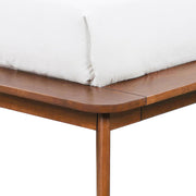 Left facing close up view of the rails and leg on a mid-century modern walnut and beige boucle wingback queen bed on a white background