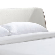 Right facing close up view of the headboard on a mid-century modern walnut and beige boucle wingback queen bed on a white background