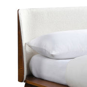 Right facing close up view of the headboard on a mid-century modern walnut and beige boucle wingback queen bed on a white background