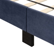 Right facing close up of the upholstered rail and wooden leg on a contemporary grey upholstered full bed with attached storage bench on a white background