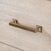 Left facing close up of the bar drawer pull on a transitional light oak five-drawer chest with a metal base