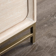 Right facing close up of the metal base on a transitional light oak eastern king platform bed with two storage drawers, in a room