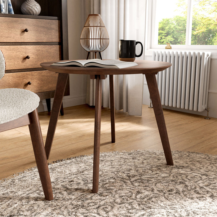 Right facing mid-century modern walnut finish round wood side table with splayed legs in a room with accessories
