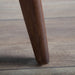Right facing close up of the leg of a mid-century modern walnut and ivory boucle accent armchair in a room