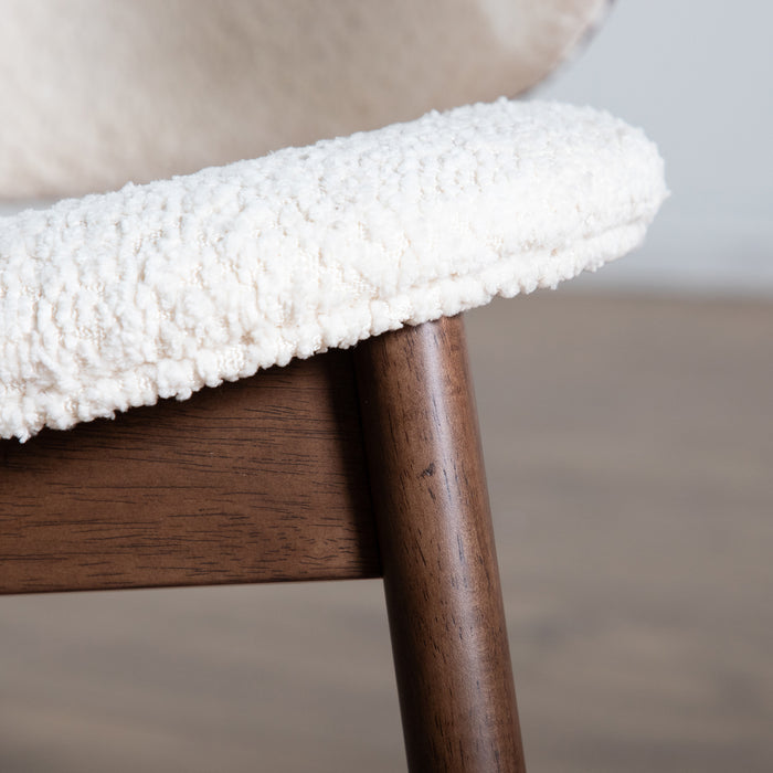 Front facing close up of the seat and upper leg of a mid-century modern walnut and ivory boucle accent armchair in a room