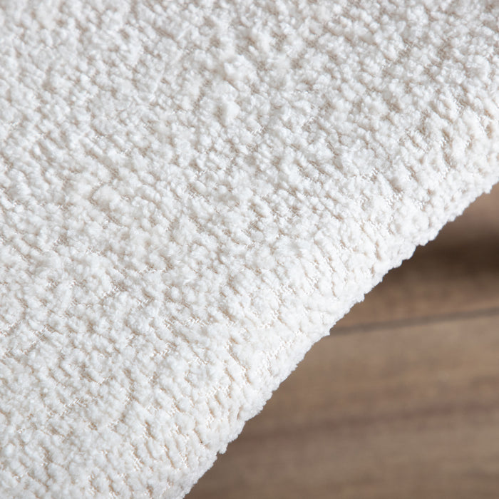 Right facing close up of the upholstery of a mid-century modern walnut and ivory boucle accent armchair in a room