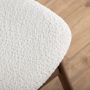 Right facing close up of the seat of a mid-century modern walnut and ivory boucle wingback accent chair in a room