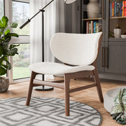 Left facing mid-century modern walnut and ivory boucle wingback accent chair in a room with accessories
