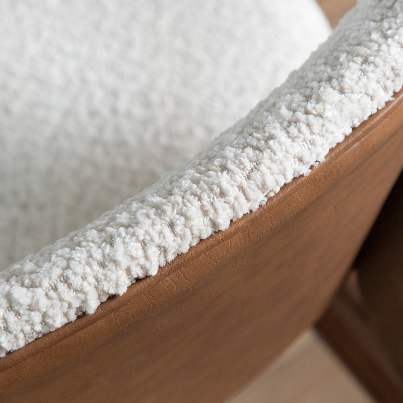 Left facing close up of the backrest of a mid-century modern walnut and ivory boucle wingback accent chair in a room