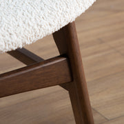 Right facing close up of the leg and support stretcher of a mid-century modern walnut and ivory boucle wingback accent chair in a room