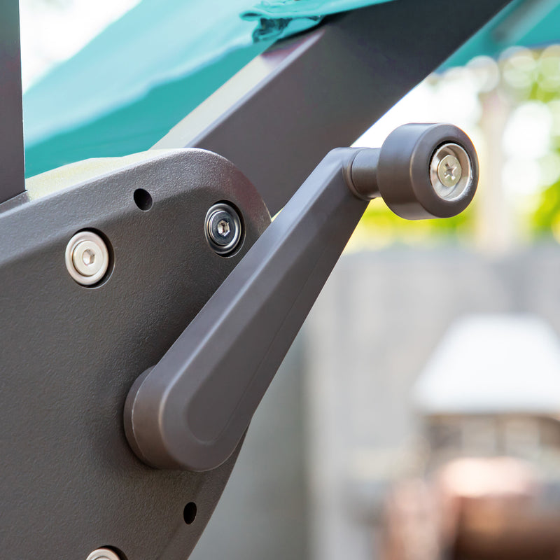 Left facing close up of the crank mechanism on a contemporary cantilever umbrella in teal fabric with solar LED lighting and carrying case on a patio