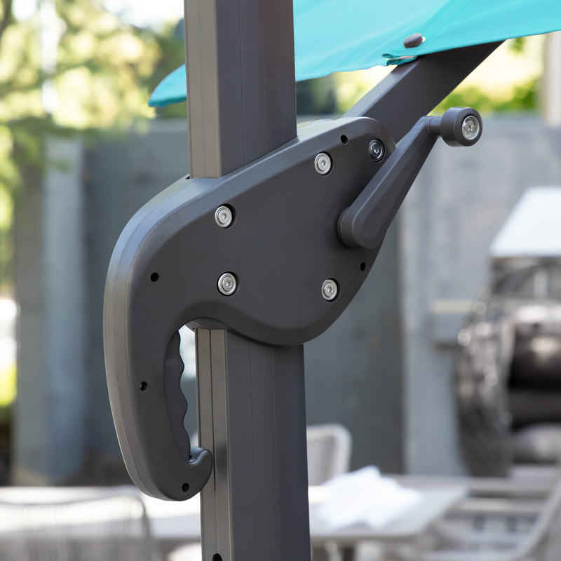 Right facing close up of the crank mechanism on a contemporary cantilever umbrella in teal fabric with solar LED lighting and carrying case on a patio