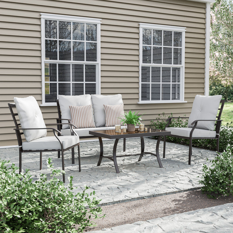 Right facing four-piece transitional beige outdoor patio seating set with a table, two chairs, and a loveseat on a patio with accessories