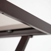 Close up of the tabletop edge of a four-piece transitional beige outdoor patio seating set with a table, two chairs, and a loveseat on a white background