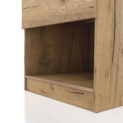 Left facing close up view of the lower shelf compartment on a rustic light oak one-drawer nightstand with an open shelf and a charging port in the tabletop on a white background