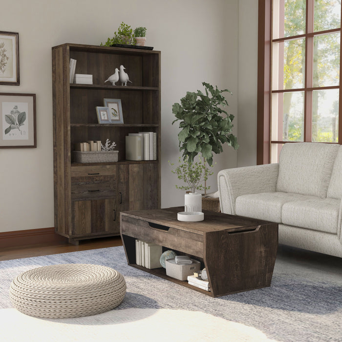 Angled view of a reclaimed oak storage coffee table and bookcase set in a modern farmhouse style living room. The chest-like coffee table, in front of the beige loveseat, features an open shelf on the base frame displaying books and a basket. Three spacious shelves on the bookcase display more books and decor. An indoor tree cushions the corner between the bookcase and loveseat, while a round rattan floor ottoman sits in the foreground of the coffee table.