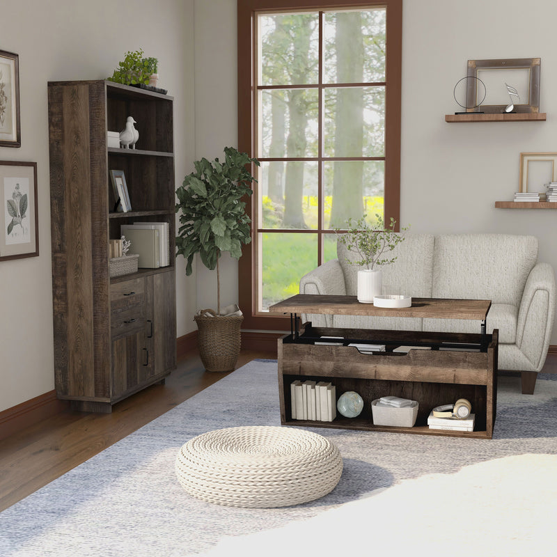 Side view of a reclaimed oak storage coffee table and bookcase set in a modern farmhouse style living room. The chest-like coffee table, in front of the beige loveseat, features a lift-top shelf with two storage compartments. The open shelf on the base frame also displays books and a basket. Three spacious shelves on the bookcase display more books and decor. An indoor tree cushions the corner between the bookcase and loveseat, while a round rattan floor ottoman sits in the foreground of the coffee table.