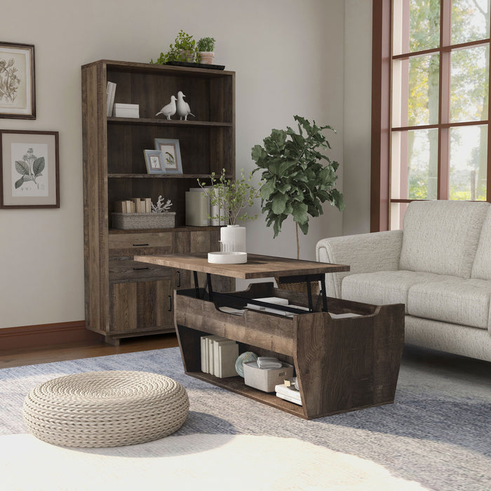 Angled view of a reclaimed oak storage coffee table and bookcase set in a modern farmhouse style living room. The chest-like coffee table, in front of the beige loveseat, features a lift-top shelf with two storage compartments. The open shelf on the base frame also displays books and a basket. Three spacious shelves on the bookcase display more books and decor. An indoor tree cushions the corner between the bookcase and loveseat, while a round rattan floor ottoman sits in the foreground of the coffee table.