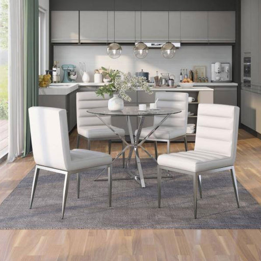 A round glass-top dining table on a chrome frame surrounded by four white leatherette upholstered chairs on chrome tapered legs. The chair backrests and seats display deep horizontal tufts.