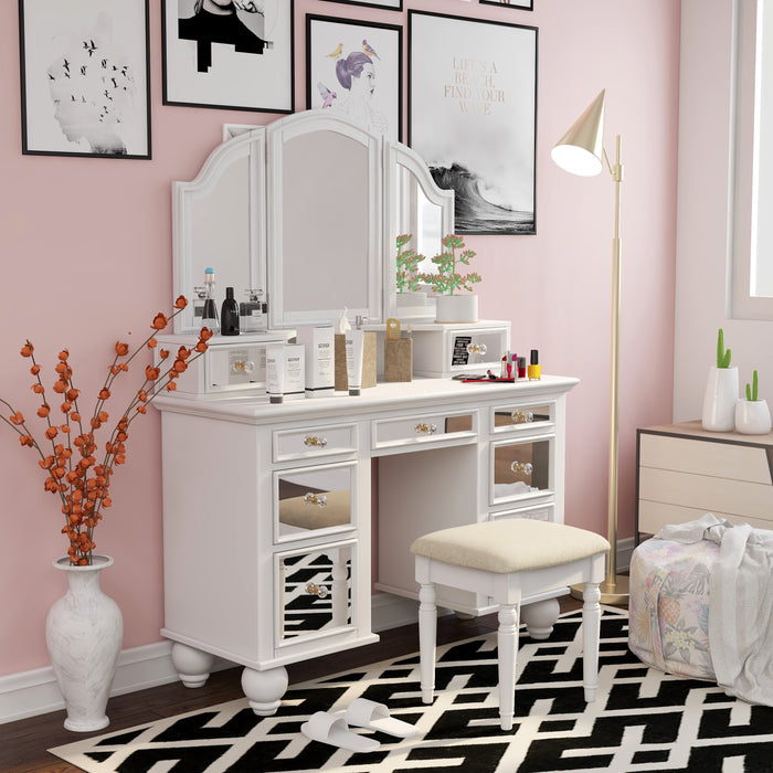Right-angled white vanity set in a pink youth bedroom. Make-up and creams adorn the vanity table. The stool sits on a black and white patterned rug that ties in with the black-framed art surrounding the mirror. A gold floor lamp, on the right, shines a light on the vanity table.