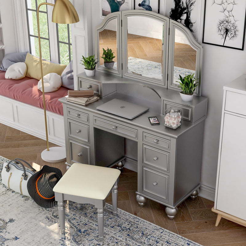 Top view of a silver vanity set in a chic teen bedroom. A laptop, iphone, and plants sit on the vanity table. To the left is a bay window seat.