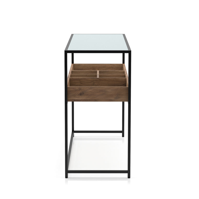 Side angle of a mixed material console table against a white background. A matte black steel frame holds a glass top for an open and airy design. Below the tabletop is a compartmentalized shelf. Two large compartments flank four smaller compartments in a warm wood color.