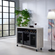 Left-angled cement and black wine bar cabinet against a white background. The 10 slots beneath the tabletop hold wine bottles, while the 3 stemware racks hang wine glasses. A plank-style drawer is flanked by wire-mesh cabinets. The entire buffet sits on wheels with parking brakes.