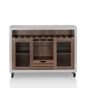 Straight-facing cement and distressed walnut wine bar cabinet against a white background. The 10 slots beneath the tabletop hold wine bottles, while the 3 stemware racks hang wine glasses. A plank-style drawer is flanked by wire-mesh cabinets. The entire buffet sits on wheels with parking brakes