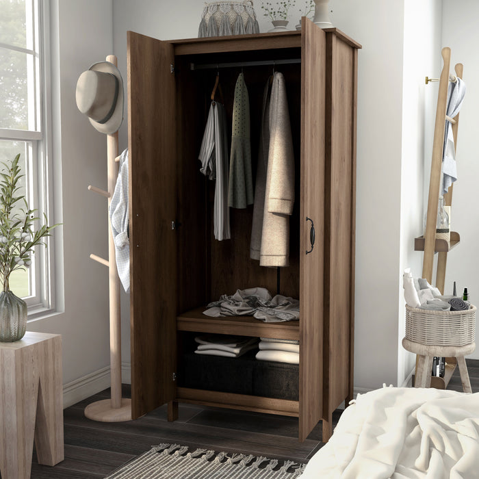 Left-angled tall, distressed walnut wardrobe cabinet with two open doors in a casual bedroom with accessories