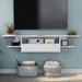 Front-facing modern white floating TV console with three shelves installed on the wall of a living room with accessories