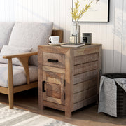 Left-angled solid mango wood side table in a beach house. The unfinished sawblade design and black bar pulls add a casual look to the shiplap white wall. A black frame hangs above the end table while a black basket sits to its right. A vase of yellow flowers, a book, and a macchiato sit on the table next to a sofa.