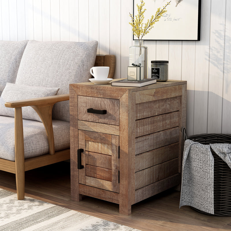 Left-angled solid mango wood side table in a beach house. The unfinished sawblade design and black bar pulls add a casual look to the shiplap white wall. A black frame hangs above the end table while a black basket sits to its right. A vase of yellow flowers, a book, and a macchiato sit on the table next to a sofa.
