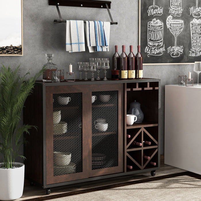 Right-angled vintage walnut wine bar cabinet in a country farmhouse style dining room. A lamp and decorative pumpkins sit on the tabletop. Behind the wire mesh cabinet doors are cups and plates. Orange wine glasses hang on stemware racks while wine bottles are stored in the wine rack.